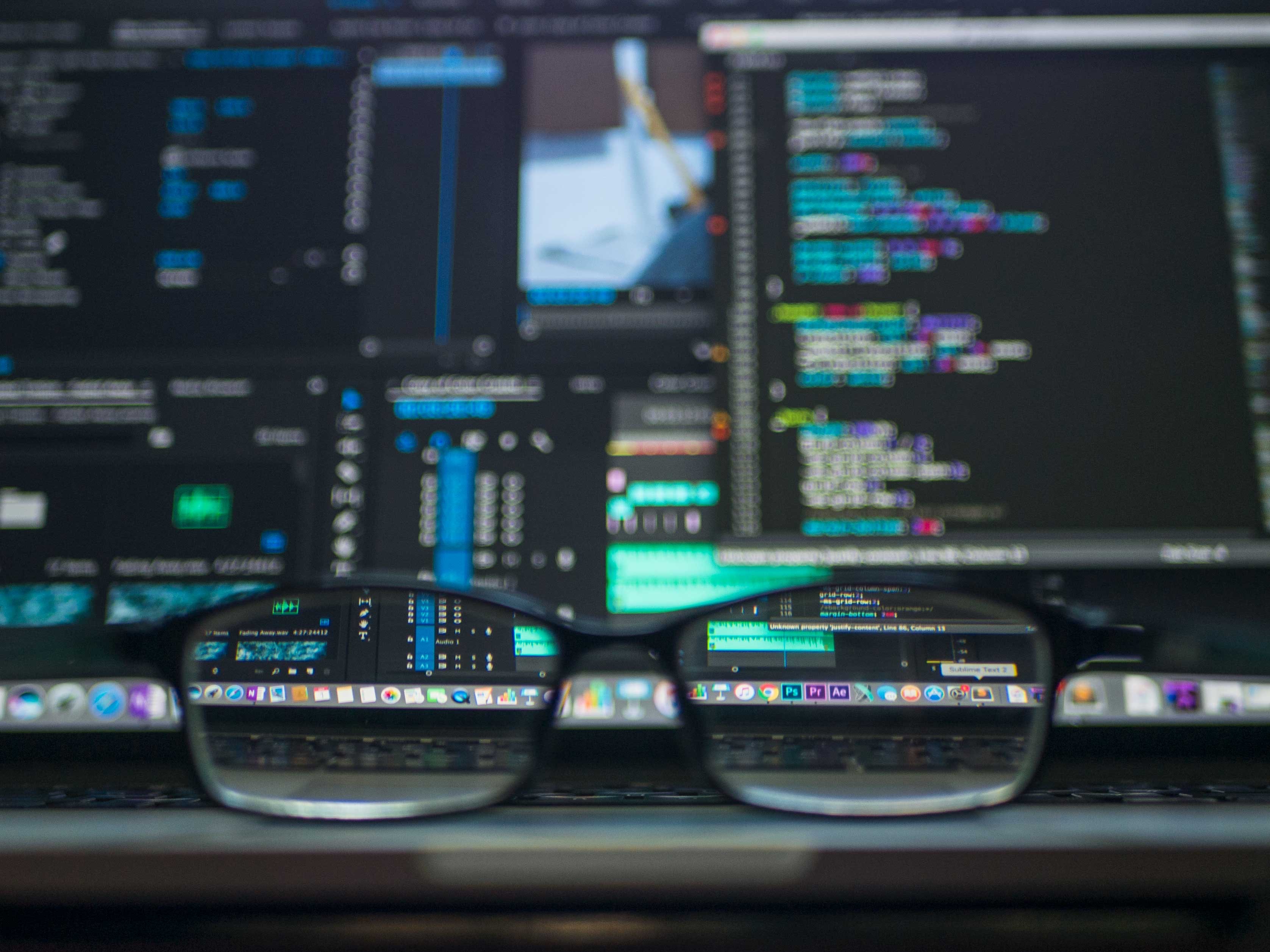 Multiple monitors with code on the screens and a pair of glasses in the forefront